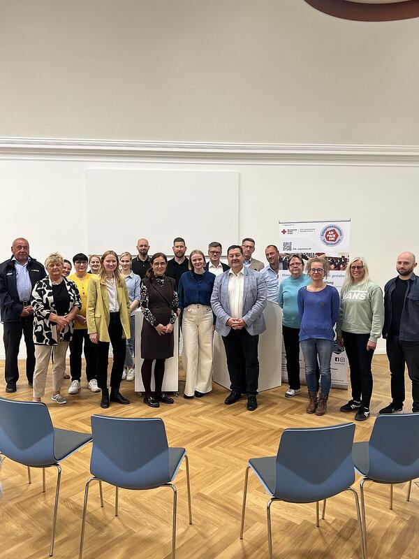 Eröffnung DRK Engagementzentrum Es steht eine Gruppe Menschen im Halbkreis vor einem Aufstelller mit dem Logo des DRK Engagementzentrum.