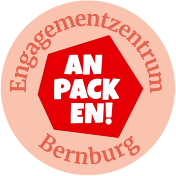 Rundes orangenes Logo, im Zentrum rotes Sechseck mit weißem Schriftzug Anpacke, im äußeren Kreis steht Engagementzentrum Bernburg 