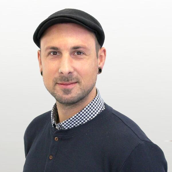 Auf dem Foto ist ein Mann mit kurzen Haaren und Mütze zu sehen, er lächelt in die Kamera. 