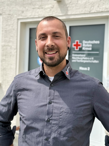 Mann mit Hemd und kurzen Haaren vor DRK Gebäude