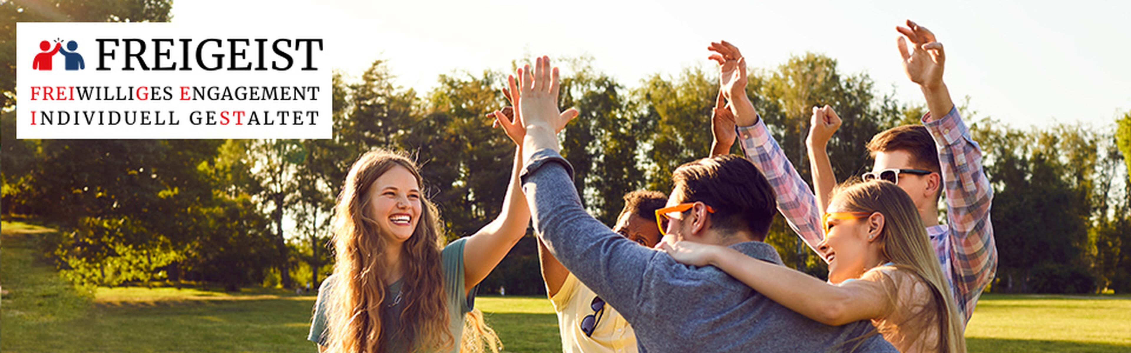 Menschen stehen in einem Kreis auf einer Wiese in der Sonne und geben sich ein High-Five und lachen. Unten links ist ein Logo von Freigeist zu sehen.