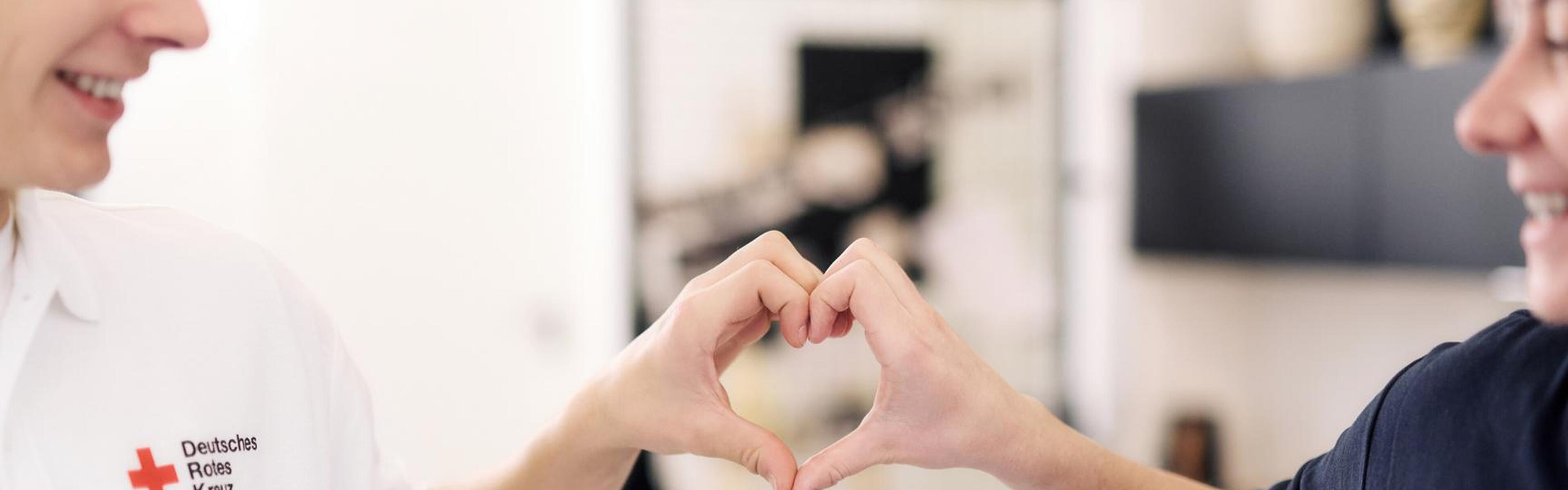 Zwei Personen formen zwischen sich mit jeweils einer Hand ein Herz