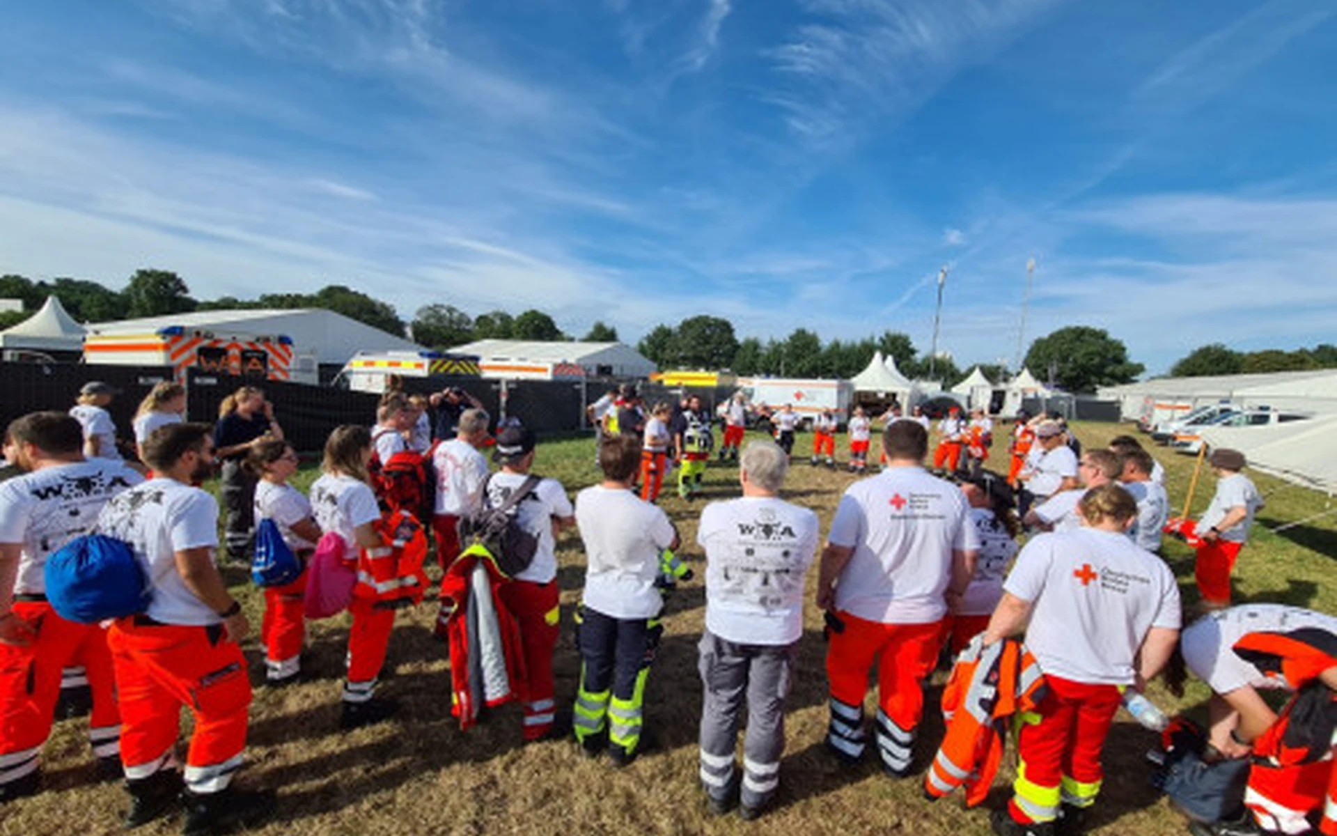 Ein grosse Gruppe DRK-Mitarbeiter und Mitarbeiterinnen bei einer Einsatzbesprechung im Freien